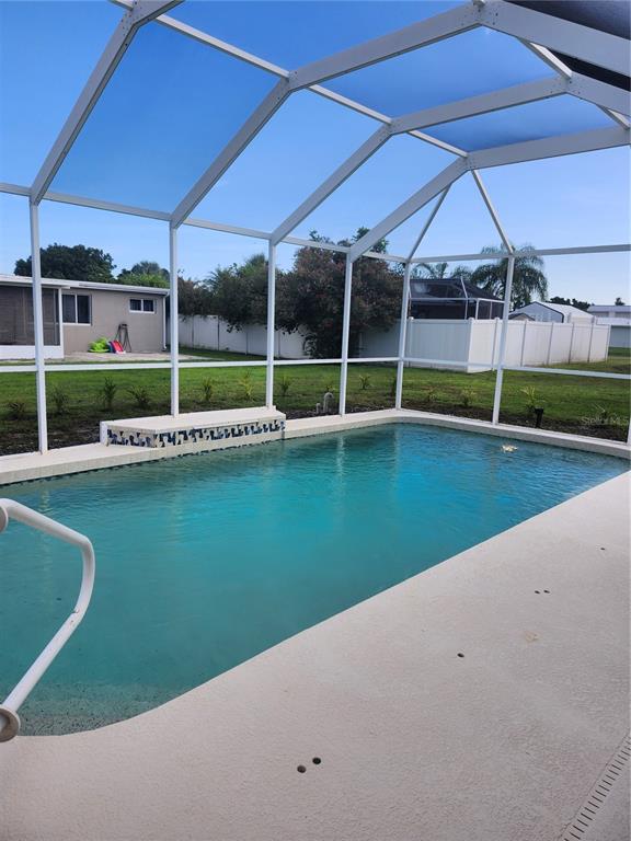 A swimming pool with a tiled ledge is enclosed by a white screen cage — 2441 BEACON DRIVE, PORT CHARLOTTE, FL