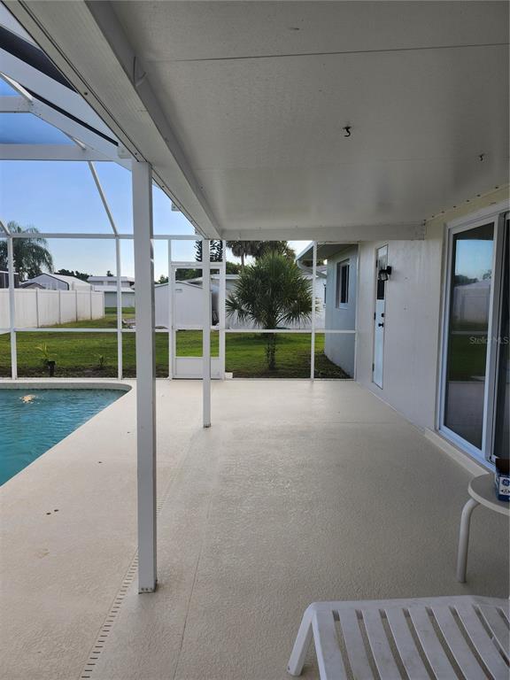 A covered patio with a pool enclosure overlooks a grassy backyard with a small palm tree — 2441 BEACON DRIVE, PORT CHARLOTTE, FL