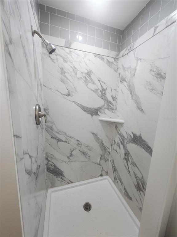 A shower stall features white marble-patterned wall panels, a white base, and gray tiled accents — 2441 BEACON DRIVE, PORT CHARLOTTE, FL