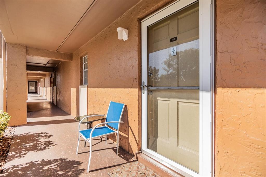 A blue patio chair sits on a concrete walkway outside a door labeled 104 — 12760 INDIAN ROCKS ROAD UNIT 104, LARGO, FL
