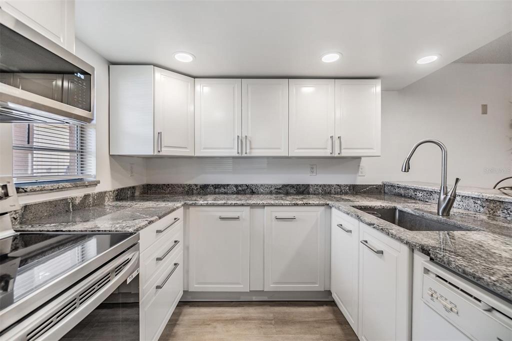 A kitchen with white cabinets, granite countertops, stainless steel appliances, and wood-look flooring — 12760 INDIAN ROCKS ROAD UNIT 104, LARGO, FL