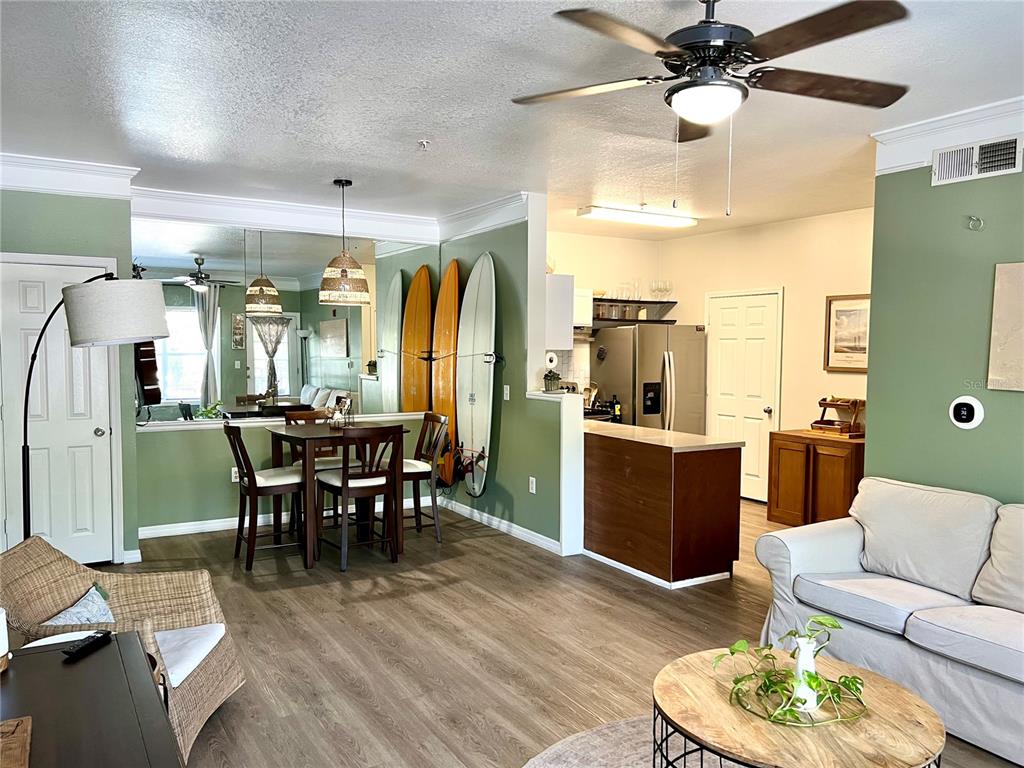An open-concept living and dining area features sage green walls, wood-look flooring, and surfboards — 4802 51ST STREET W UNIT 1315, BRADENTON, FL