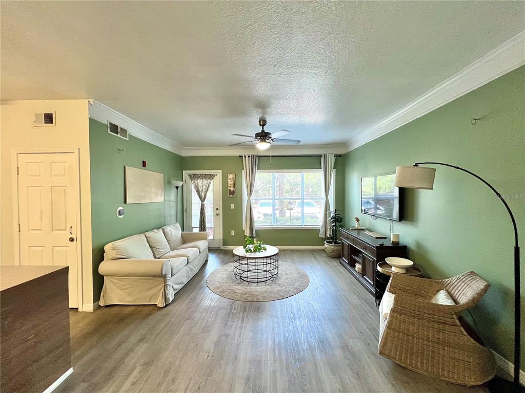 A living room features green walls, light wood-look flooring, a sofa, and a ceiling fan — 4802 51ST STREET W UNIT 1315, BRADENTON, FL