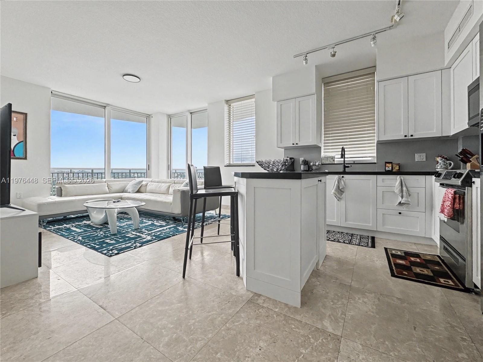 A modern open-concept kitchen and living area features white cabinetry, tile floors, and floor-to-ceiling windows — 1755 E Hallandale Beach Blvd # 2207E, Hallandale Beach FL 33009, HALLANDALE BEACH, FL