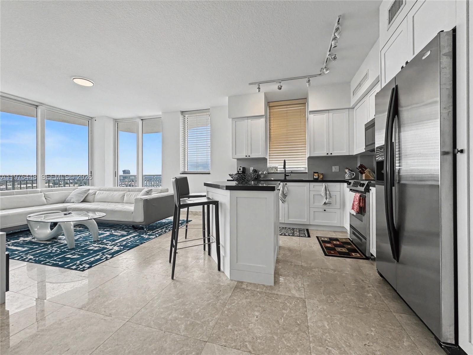 A modern open-concept kitchen and living area features white cabinetry, stainless steel appliances, and tile flooring — 1755 E Hallandale Beach Blvd # 2207E, Hallandale Beach FL 33009, HALLANDALE BEACH, FL