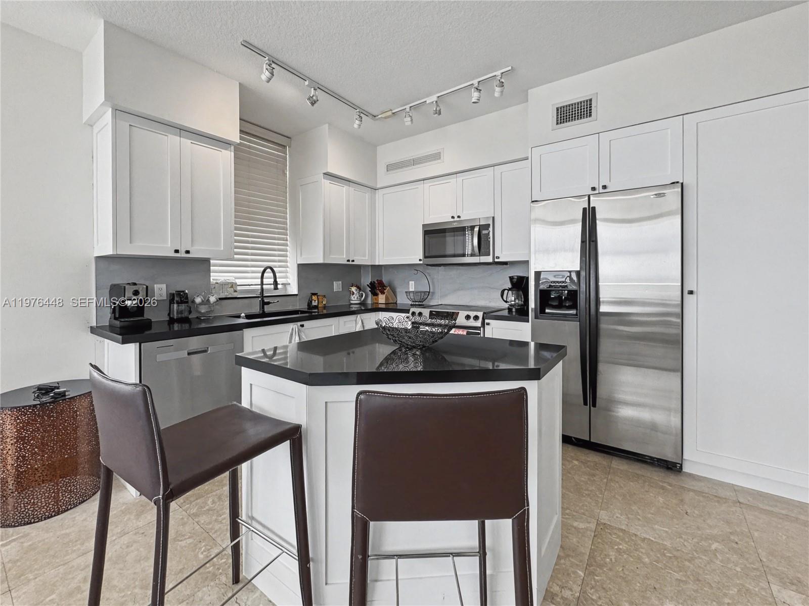 A kitchen features white cabinetry, black countertops, stainless steel appliances, and a central island — 1755 E Hallandale Beach Blvd # 2207E, Hallandale Beach FL 33009, HALLANDALE BEACH, FL