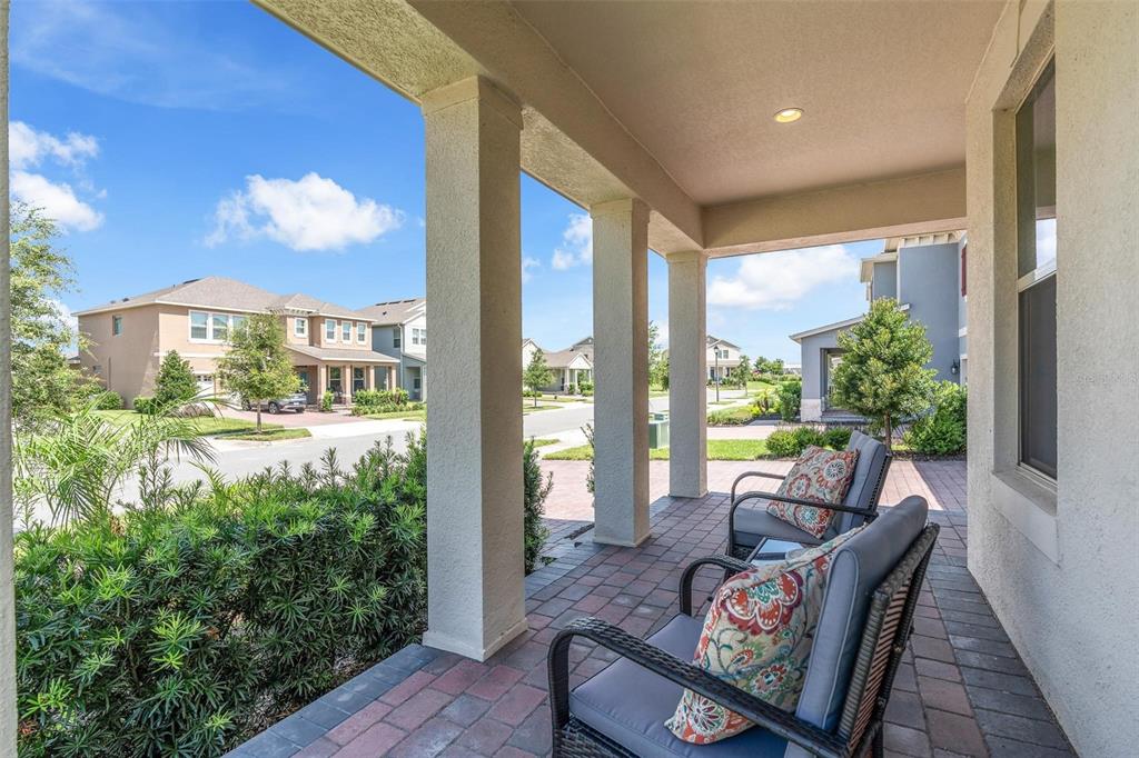 A covered front porch with brick pavers features two chairs and views of a neighborhood — 11043 JACKSON COVE, WINTER GARDEN, FL