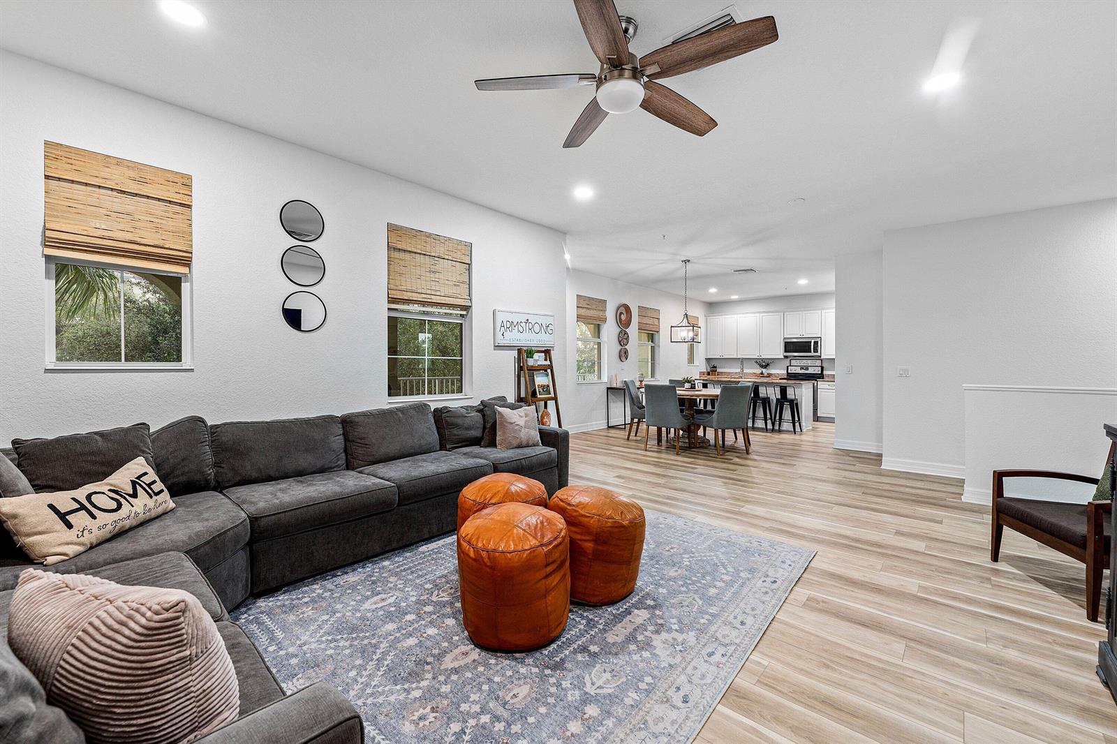 An open-concept living room features a gray sectional, leather ottomans, and a kitchen in back — 1056 Community Drive, Jupiter FL 33458, JUPITER, FL