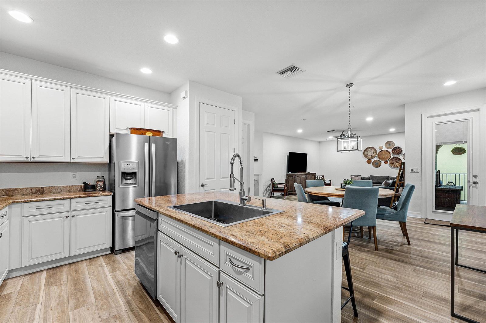 A kitchen with white cabinets, granite countertops, and an island opens to a dining area — 1056 Community Drive, Jupiter FL 33458, JUPITER, FL