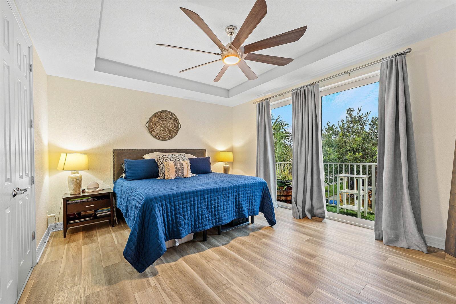 A bedroom with a blue bed, wood-look flooring, a ceiling fan, and a balcony door — 1056 Community Drive, Jupiter FL 33458, JUPITER, FL