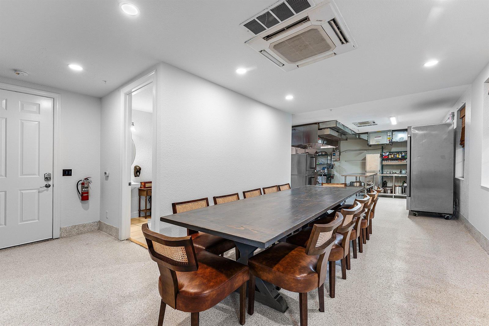 A dining room features a long wooden table with leather chairs and an adjacent kitchen — 1056 Community Drive, Jupiter FL 33458, JUPITER, FL
