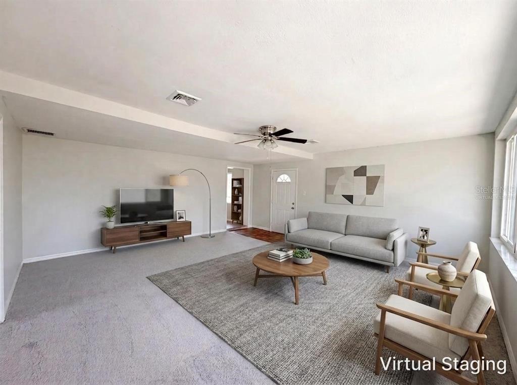 A living room with gray carpet, a sofa, two armchairs, and a television console — 900 OAK DRIVE, LEESBURG, FL