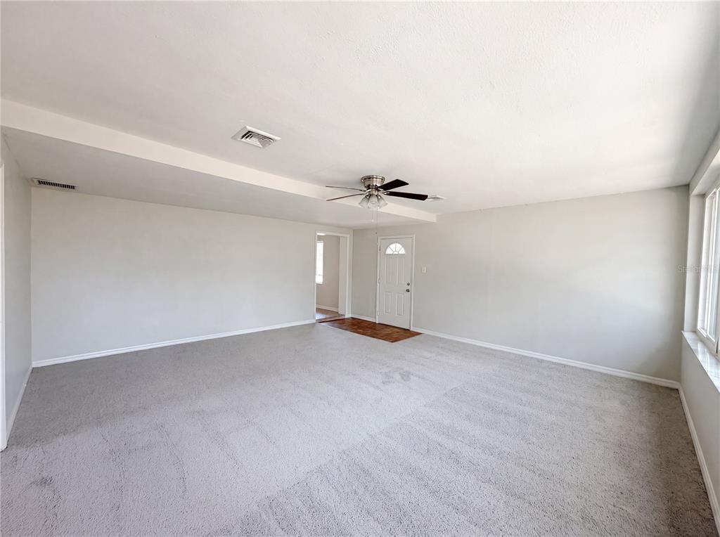 A spacious living room with gray carpet, white walls, a ceiling fan, and an entryway — 900 OAK DRIVE, LEESBURG, FL