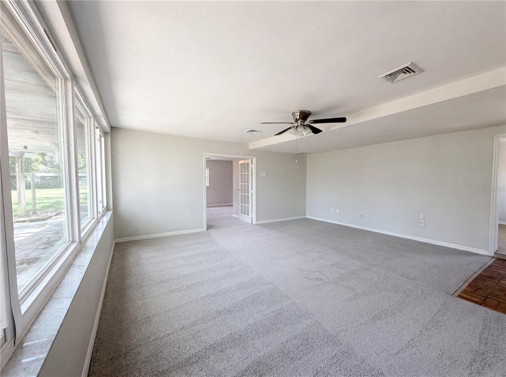 A spacious living room features gray carpeting, a ceiling fan, and large windows — 900 OAK DRIVE, LEESBURG, FL