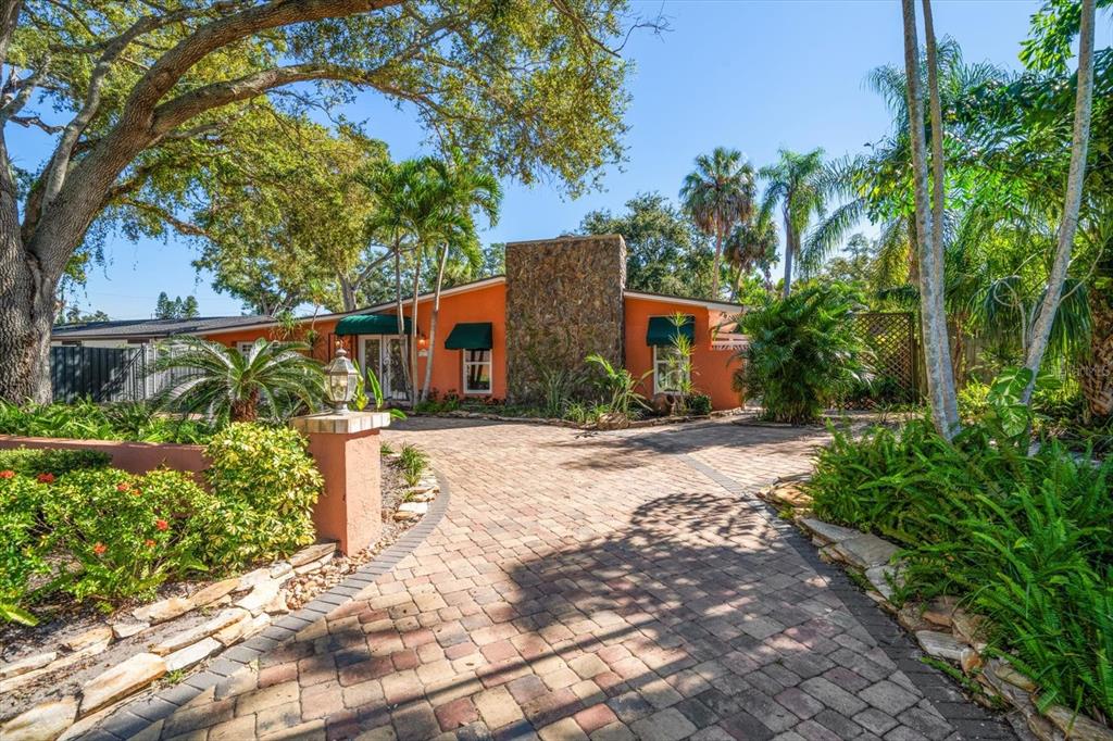 A single-story orange house with a stone chimney and a brick paver driveway — 3033 82ND WAY N, ST PETERSBURG, FL