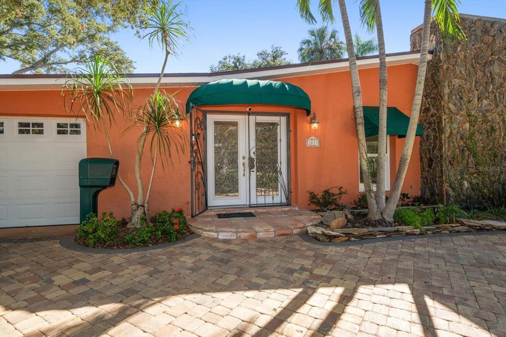 The exterior of a house features an orange stucco facade, a stone wall, and awnings — 3033 82ND WAY N, ST PETERSBURG, FL