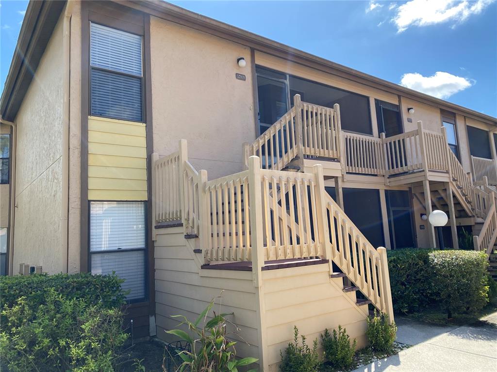 An exterior view of a two-story apartment building with wooden stairs leading to a balcony — 5769 AVISTA DRIVE UNIT 5769, SARASOTA, FL