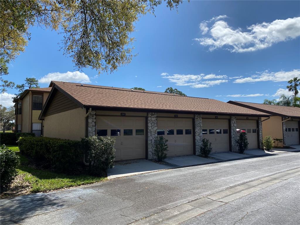 A row of four tan garage doors with stone accents under a brown shingled roof — 5769 AVISTA DRIVE UNIT 5769, SARASOTA, FL