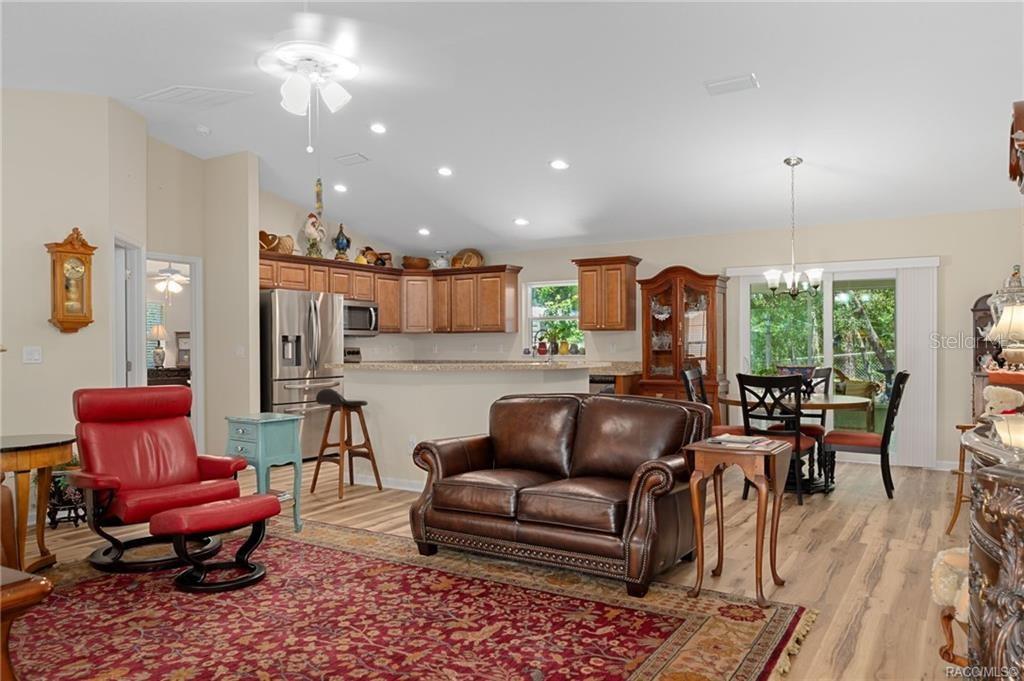 An open-concept living room and kitchen featuring wood-look flooring, a leather sofa, and red chair — 8429 N TINY LILY DRIVE, CITRUS SPRINGS, FL