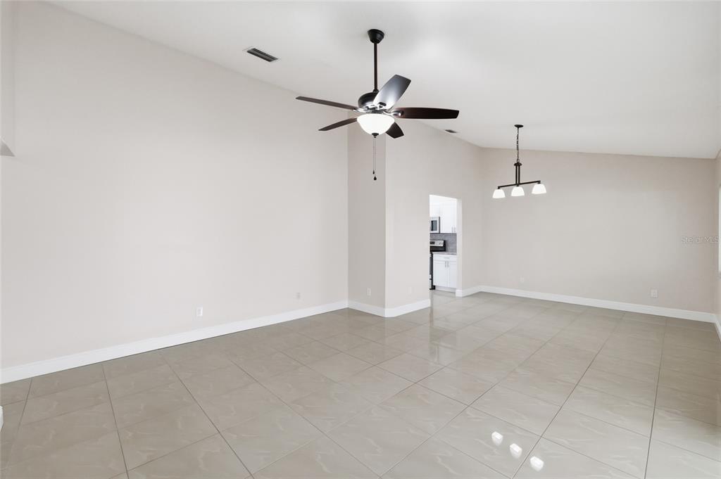 A spacious, empty room features light-colored tile flooring, a ceiling fan, and a hanging light fixture — 11807 NICKLAUS CIRCLE, TAMPA, FL
