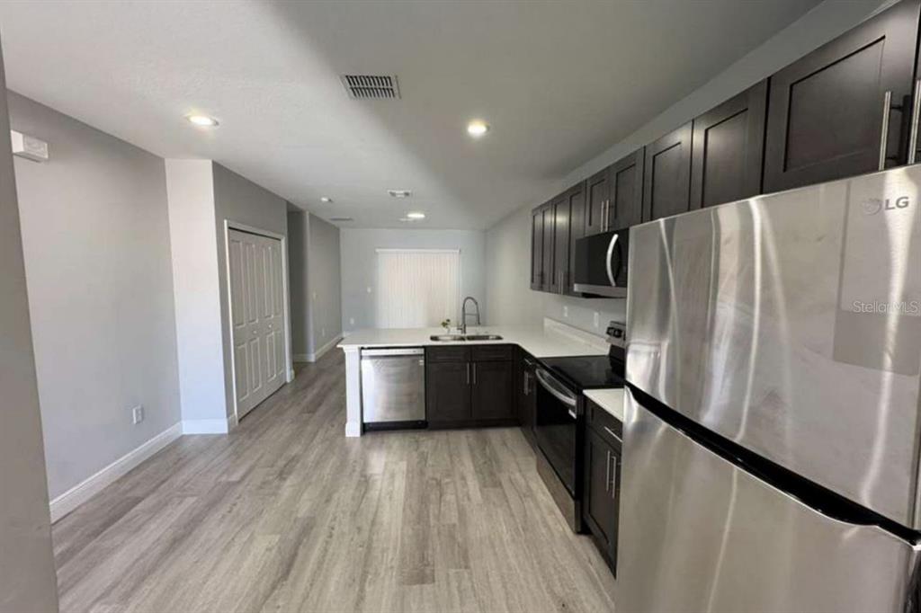 A modern kitchen features dark wood cabinets, stainless steel appliances, and light wood-look flooring — 987 NW 57TH COURT UNIT A, OCALA, FL
