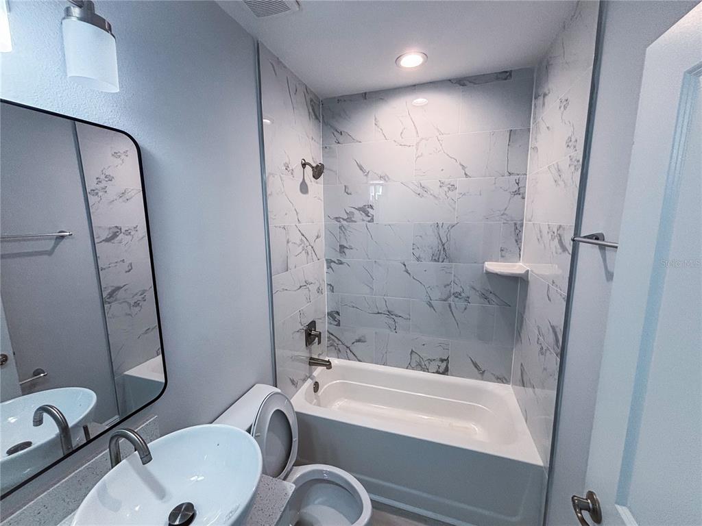 A bathroom features a vessel sink, a mirror, and a bathtub with marble-patterned tile walls — 987 NW 57TH COURT UNIT A, OCALA, FL