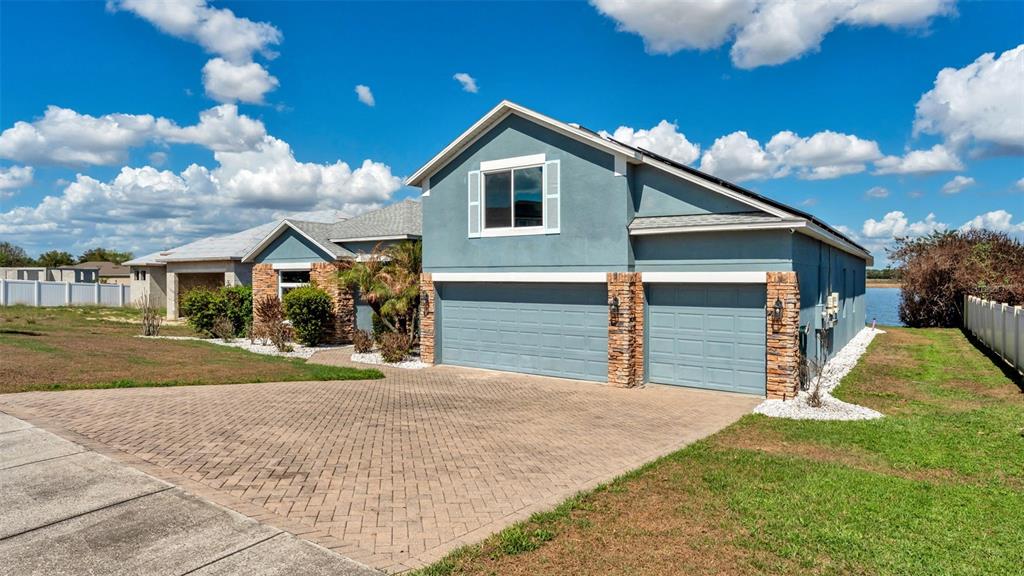 A blue house with a stone-accented three-car garage and a paved driveway under a sky — 4530 BROOKSHIRE PLACE, LAKE WALES, FL