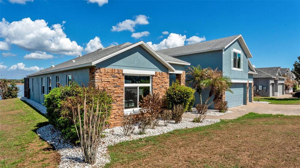 A blue house with stone accents and a white gravel garden sits near a lake — 4530 BROOKSHIRE PLACE, LAKE WALES, FL