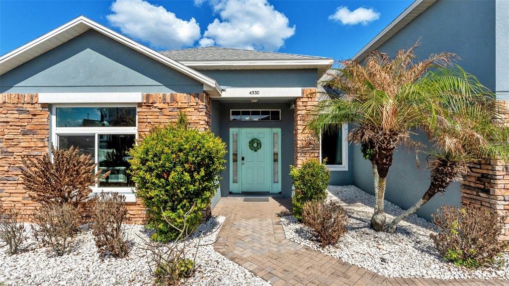 The exterior of a house features a light blue door, stone siding, and a palm tree — 4530 BROOKSHIRE PLACE, LAKE WALES, FL