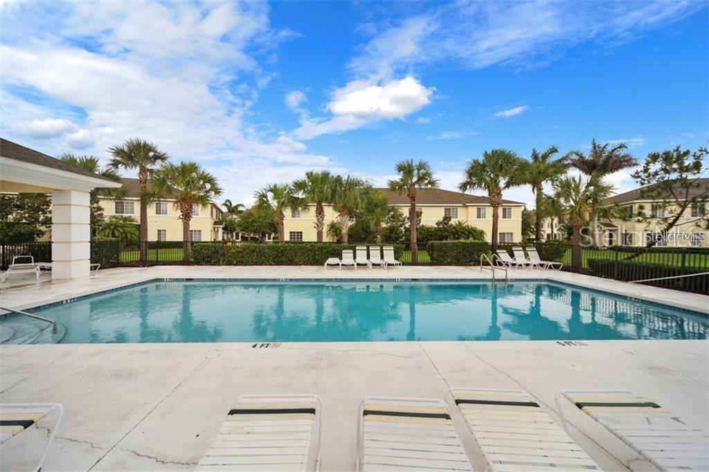 A rectangular swimming pool sits on a concrete deck surrounded by palm trees and buildings — 267 CAPE HARBOUR LOOP UNIT 101, BRADENTON, FL