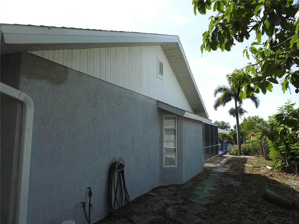 The exterior side of a house features gray stucco walls, white siding, and a window — 2132 PENNSYLVANIA AVENUE, ENGLEWOOD, FL
