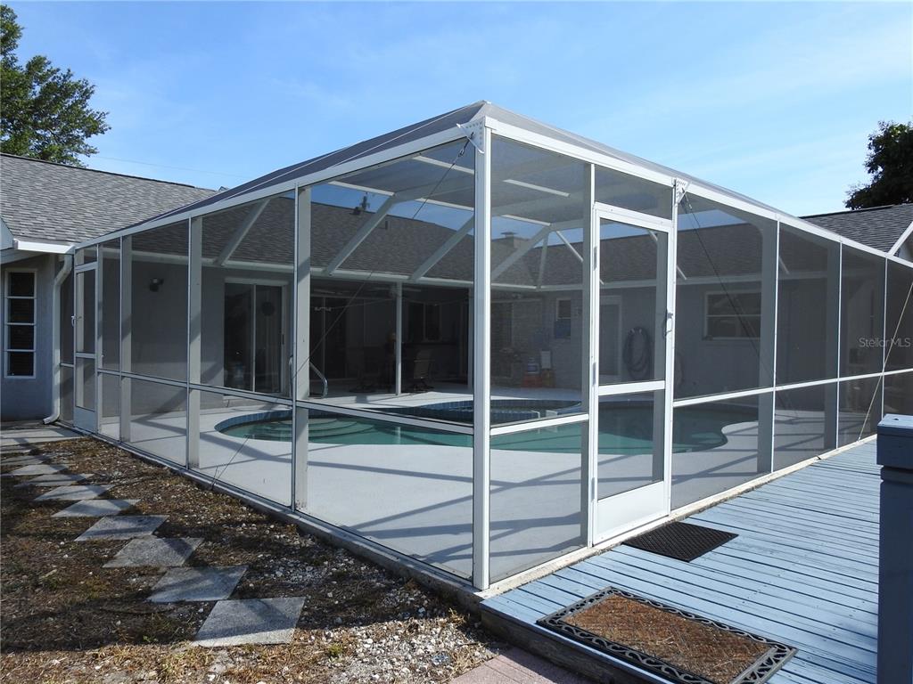 A swimming pool is enclosed by a white-framed screen structure next to a wooden deck — 2132 PENNSYLVANIA AVENUE, ENGLEWOOD, FL