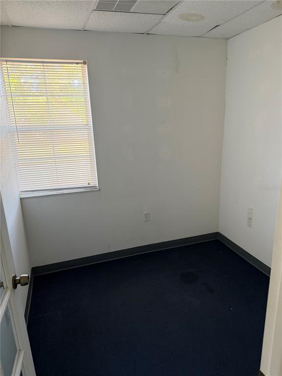 An empty room features white walls, a window with blinds, and dark blue carpeting — 15500 GEORGE BOULEVARD, CLEARWATER, FL