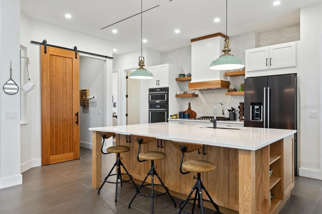 A modern kitchen features a large wooden island, white cabinets, and a sliding barn door — 3705 RIDGE RUN DRIVE, MINNEOLA, FL