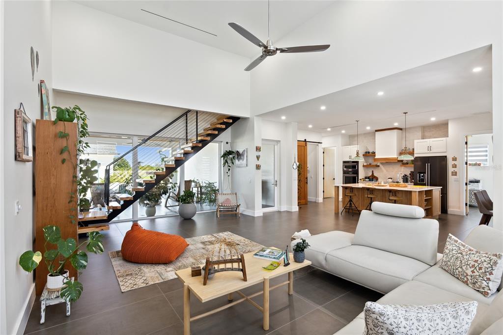 An open-concept living room features a floating staircase, a white sofa, and a modern kitchen — 3705 RIDGE RUN DRIVE, MINNEOLA, FL