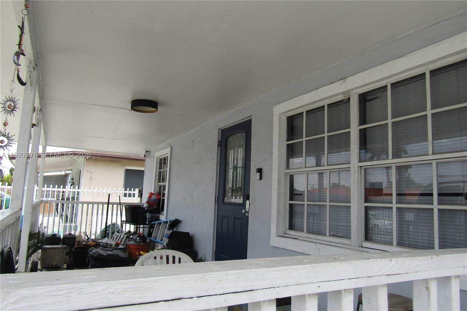 A covered front porch features a blue door, white railings, and various stored items — 2223 NW 32nd St, Miami FL 33142, MIAMI, FL