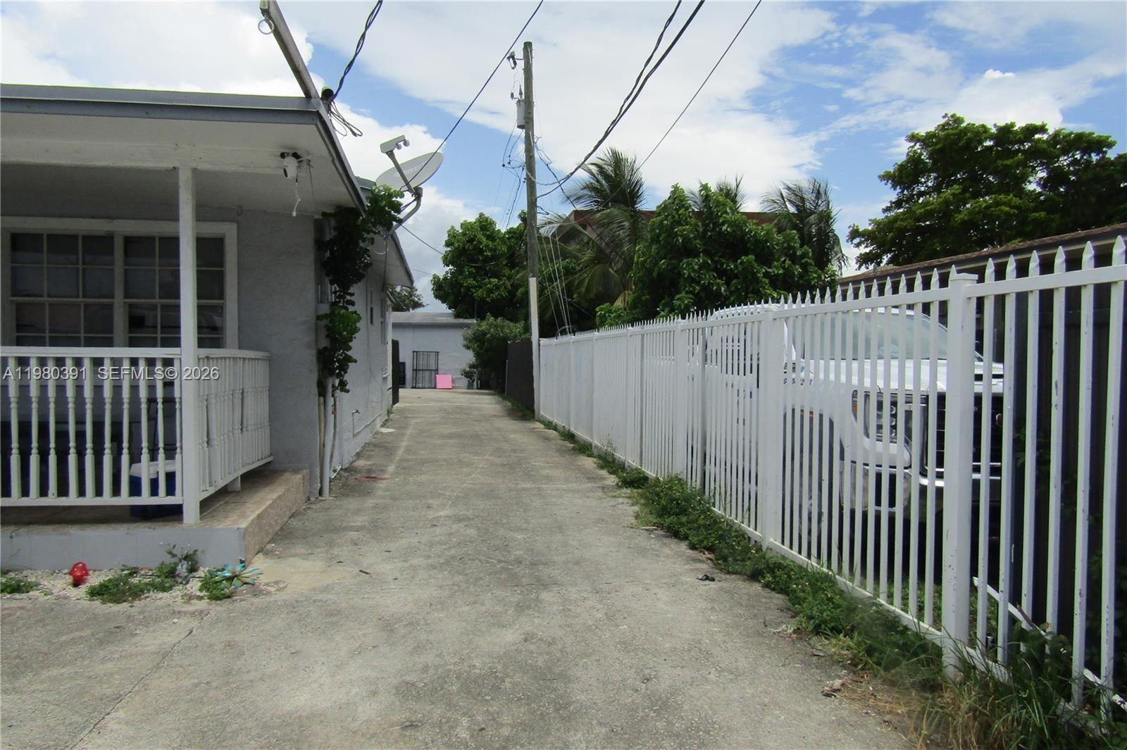 A concrete driveway runs between a house with a porch and a white metal fence — 2223 NW 32nd St, Miami FL 33142, MIAMI, FL