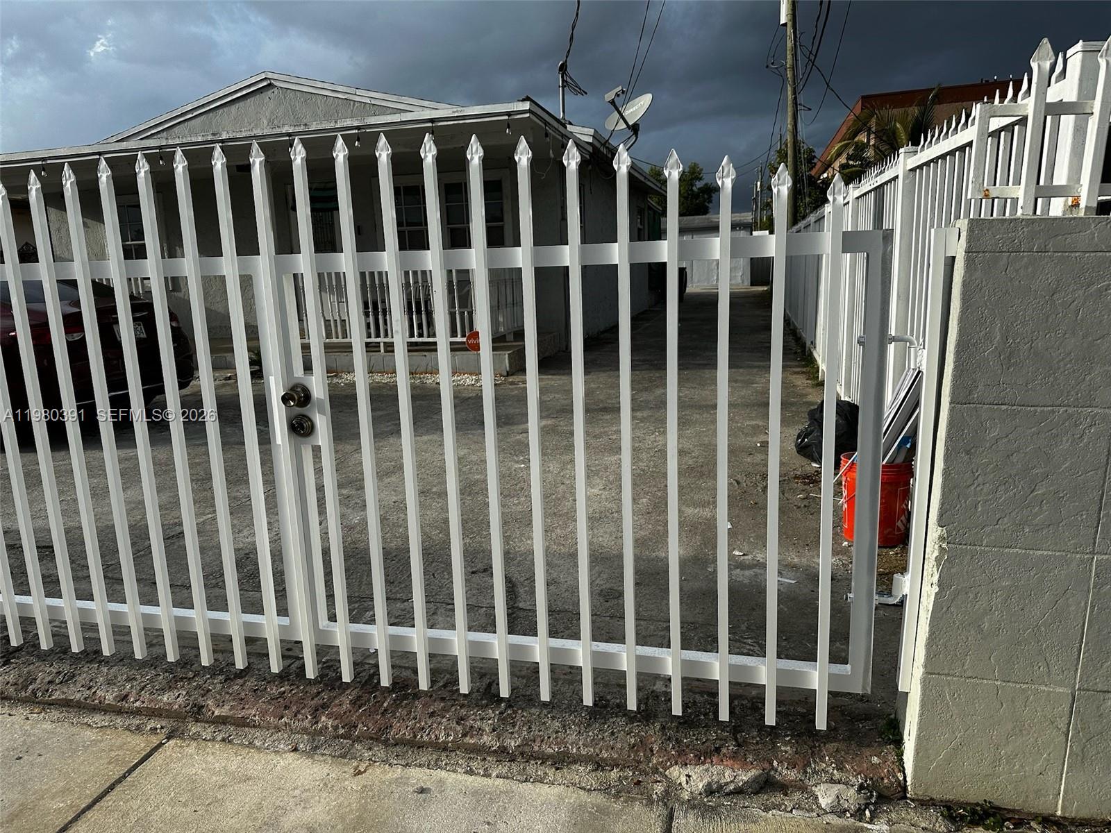 A white metal gate stands in front of a house with a concrete driveway — 2223 NW 32nd St, Miami FL 33142, MIAMI, FL