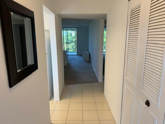 A hallway with tiled flooring leads to a carpeted living area with a balcony view — 6675 S Oriole Boulevard # 4040, Delray Beach FL 33446, DELRAY BEACH, FL