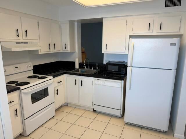 A kitchen with white cabinets, black countertops, white appliances, and light-colored floor tiles — 6675 S Oriole Boulevard # 4040, Delray Beach FL 33446, DELRAY BEACH, FL