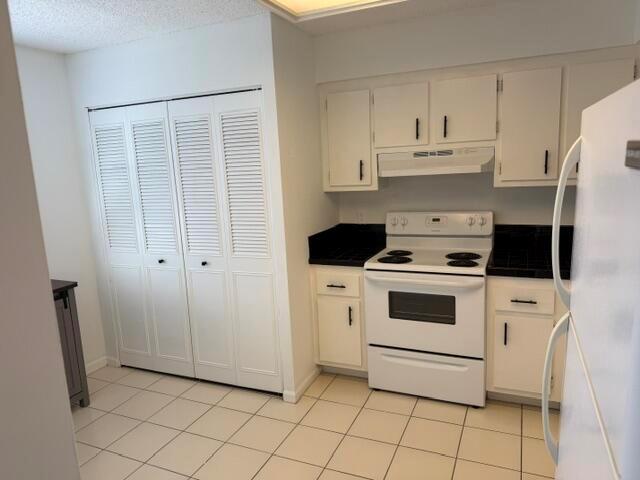 A kitchen features white cabinets, a white electric stove, black countertops, and louvered closet doors — 6675 S Oriole Boulevard # 4040, Delray Beach FL 33446, DELRAY BEACH, FL