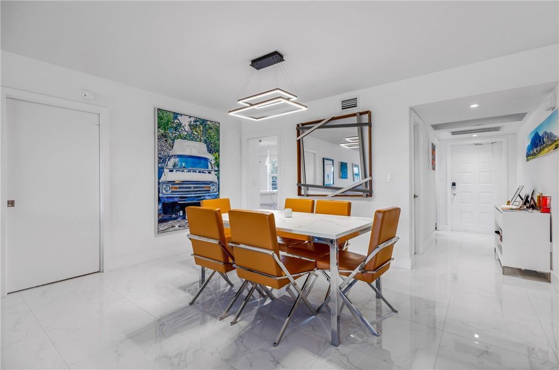 A dining room features a white marble table, orange chairs, and a modern geometric chandelier — 805 Cypress Boulevard # 210, Pompano Beach FL 33069, POMPANO BEACH, FL
