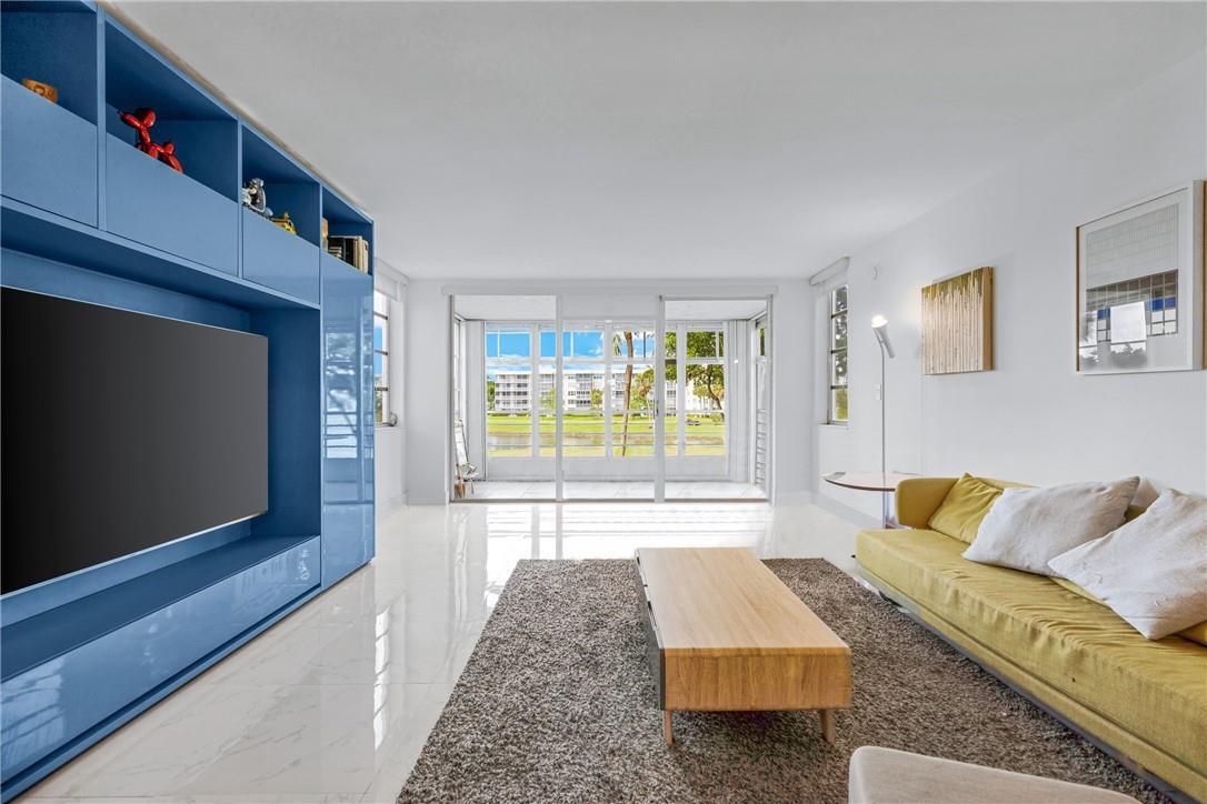 A living room features a large blue media wall, white tile floors, and a yellow sofa — 805 Cypress Boulevard # 210, Pompano Beach FL 33069, POMPANO BEACH, FL