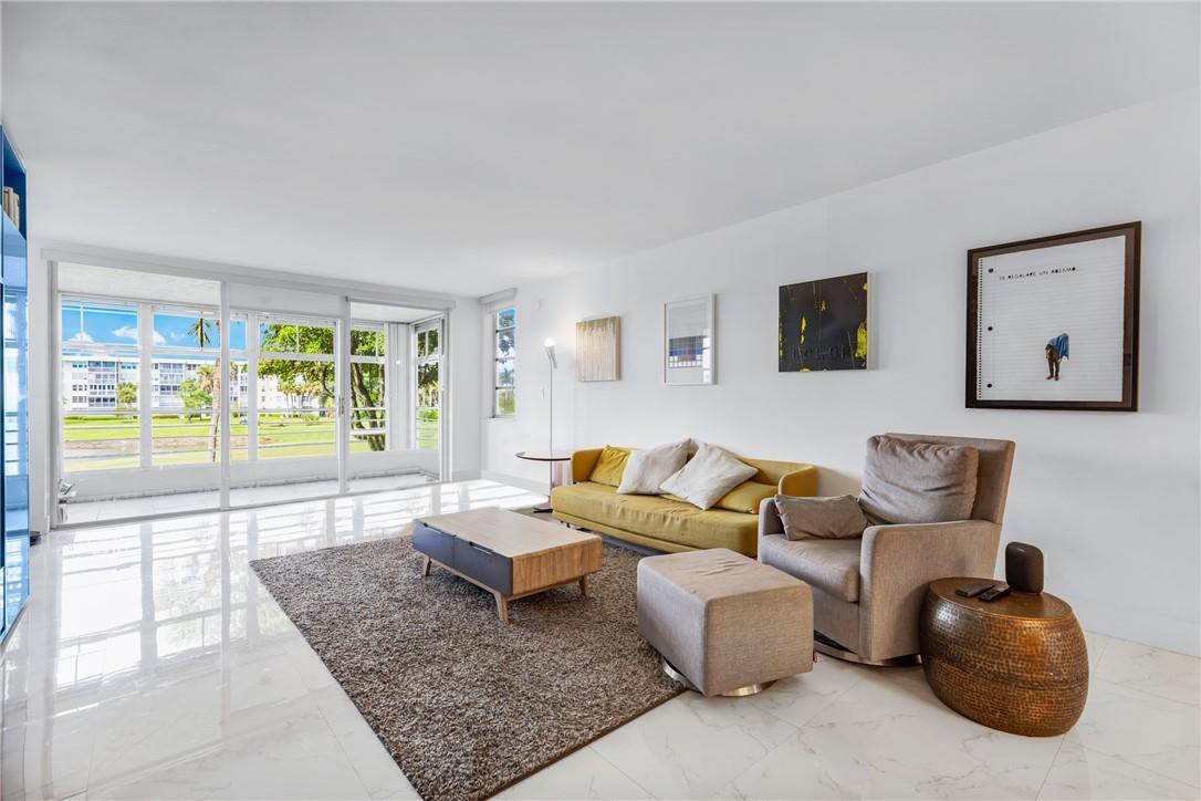 A bright living room features a yellow sofa, an armchair with ottoman, and floor-to-ceiling windows — 805 Cypress Boulevard # 210, Pompano Beach FL 33069, POMPANO BEACH, FL