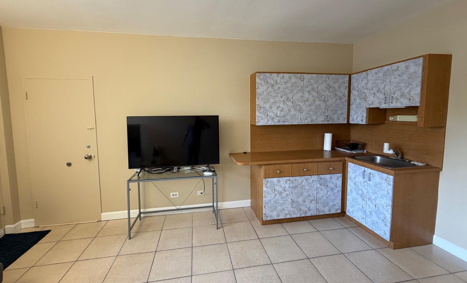 A room with beige walls, tile flooring, a television on a stand, and a kitchenette — 26 Diplomat Parkway, FL 33009, FL