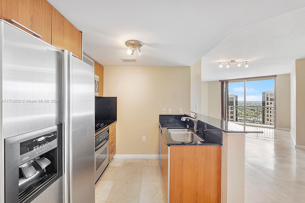 A kitchen with stainless steel appliances, dark countertops, and wood cabinets opens to a living area — 9066 SW 73rd Ct # 1904, Miami FL 33156, MIAMI, FL