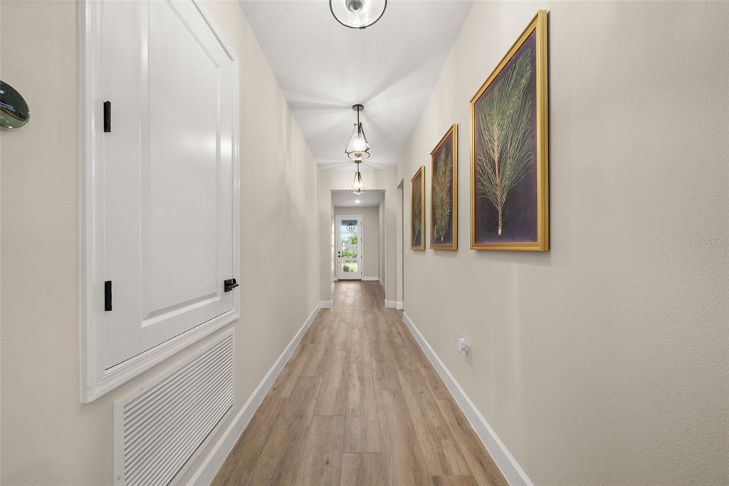 A hallway with light wood-look flooring, three framed botanical prints, and a white door — 4659 MIGNON DRIVE, SEBRING, FL