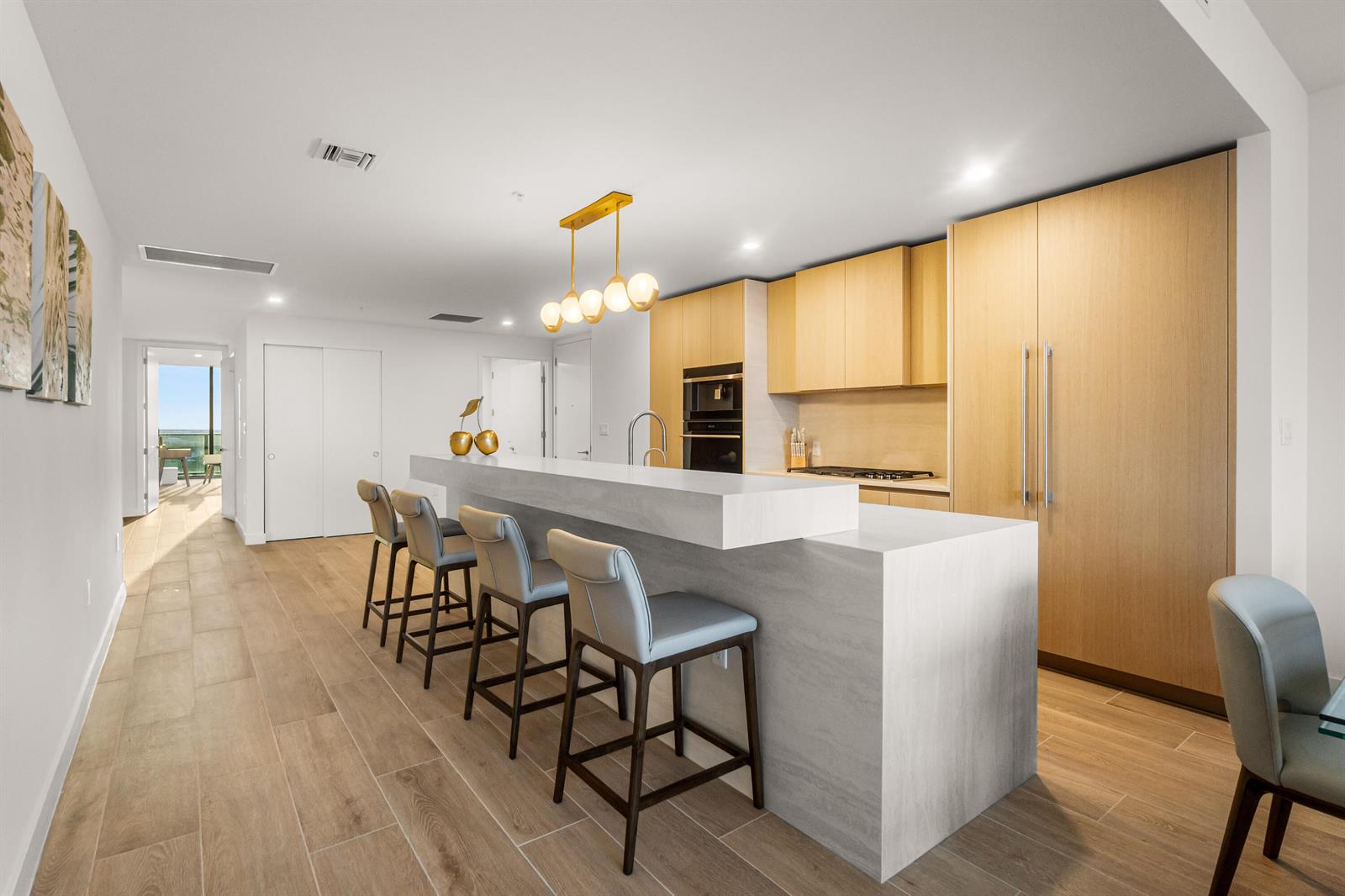 A modern kitchen features light wood cabinetry, a stone waterfall island, and four bar stools — 900 N Ocean Boulevard # 1904, Pompano Beach FL 33062, POMPANO BEACH, FL