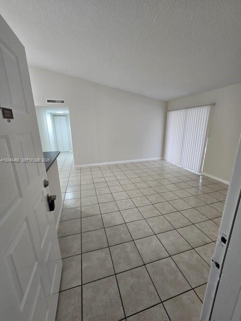 An interior view of an empty apartment living area with beige tile flooring and vertical blinds — HIALEAH, FL
