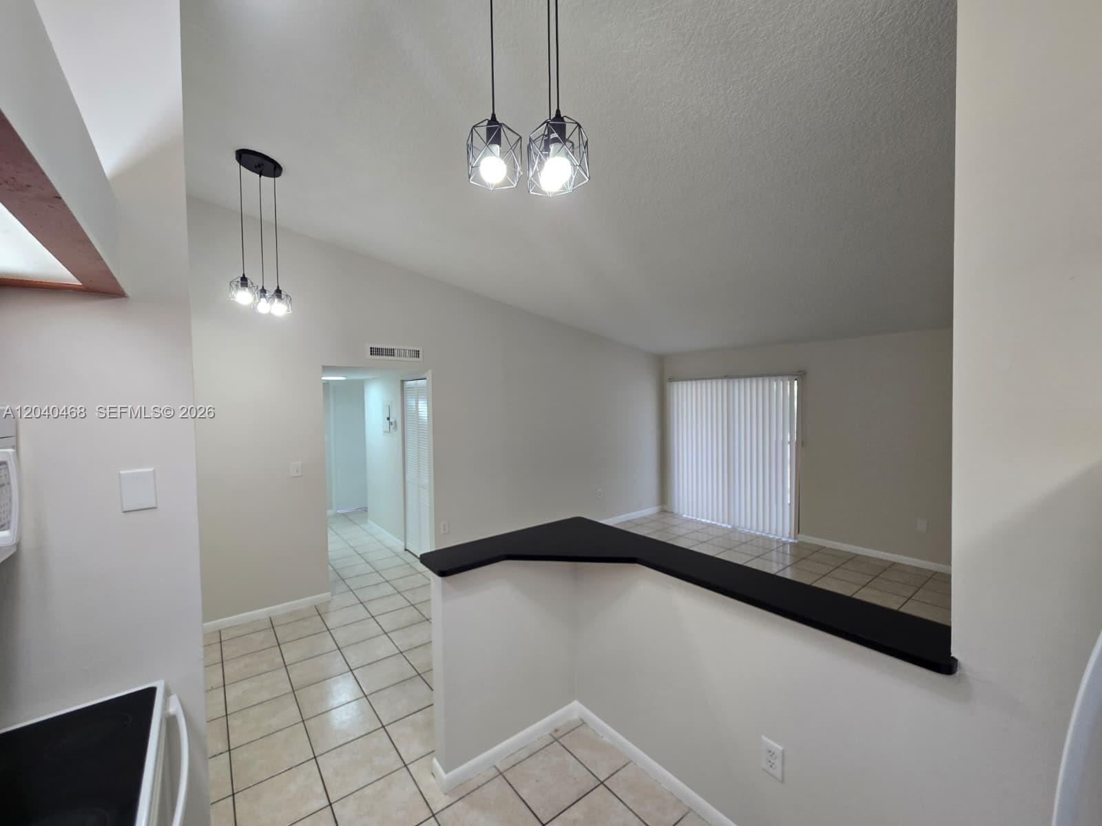 A kitchen pass-through overlooks a living area with tile floors and vaulted ceilings — HIALEAH, FL